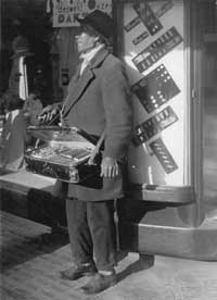 Een Chinese venter van pindakoekjes prijst in juni 1934 zijn waar aan voor het gebouw van de Bijenkorf in Den Haag